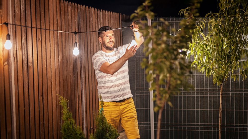 Un homme met en place des décorations lumineuses dans un jardin, ajoutant une touche magique à l'ambiance.