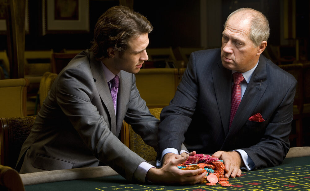 An older gentleman handing a younger man a hefty stack of casino chips